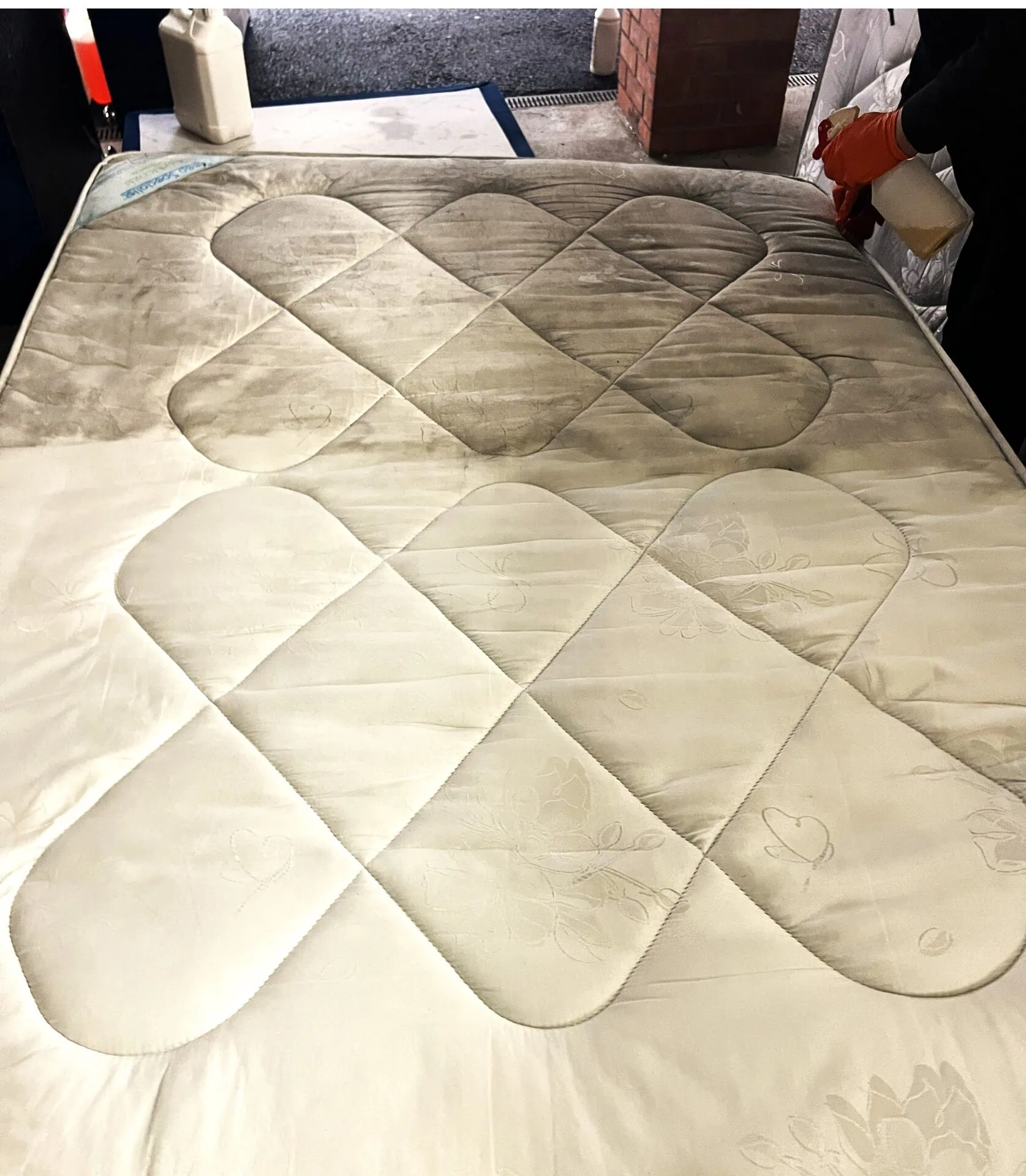 Mattress part-way through a deep clean — the top half grey with body oil and dust soiling, the cleaned lower half bright white